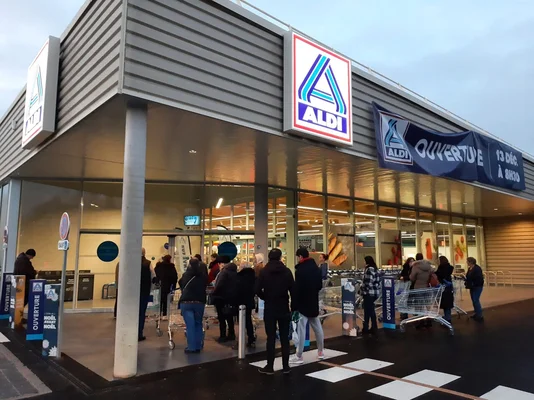 Extérieur d'un magasin Aldi près de Grenoble, clients rassemblés devant l'entrée sous des banderoles annonçant l'ouverture le 13 décembre à 8 h 30.