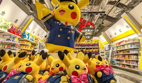 Statue géante de Pikachu en uniforme de policier bleu dans une boutique Pokémon à Tokyo, entourée de peluches Pikachu en uniforme avec nœuds roses et de rayonnages de produits dérivés.