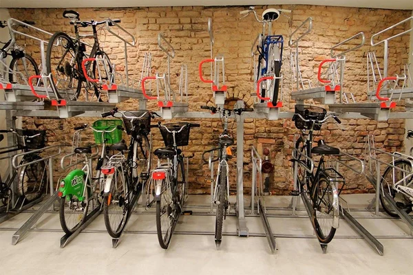 Photographie d'un système d'installation de vélos sur deux niveaux contre un mur de brique, avec plusieurs vélos garés aux étages supérieurs et inférieurs