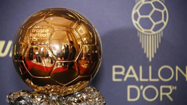 Gros plan du trophée du Ballon d'Or 2026, un ballon de football en or sur un soc de roche, posé sur un fond bleu décoré du logo et du texte de l'award, lors de la cérémonie à Londres.