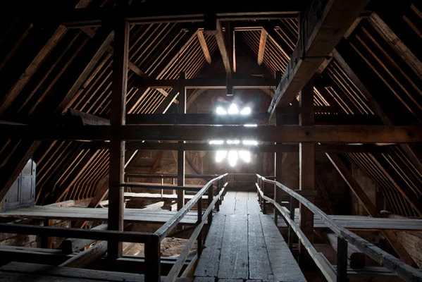 Vue intérieure de la charpente en bois de Notre-Dame de Paris, avec un passage central menant vers une lumière vive sous les combles.