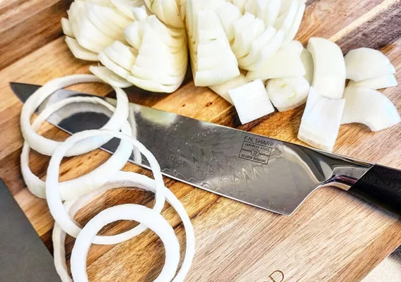 Oignons blancs émincés en rondelles et en tranches sur une planche à découper en bois, à côté de la lame d'un couteau de chef