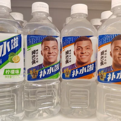 Des bouteilles d'eau en plastique sur une étagère, munies d'étiquettes présentant le visage souriant de Mao Zedong et des caractères chinois, avec des graphiques bleus et orange.