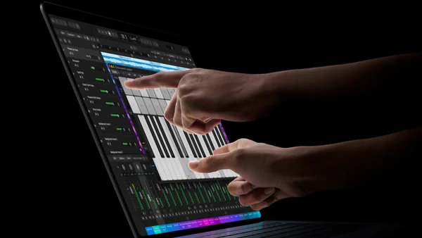 Des mains interagissent avec un écran tactile d'un MacBook Pro OLED affichant une interface de station de travail audio (DAW) et un clavier piano virtuel, illustrant l'usage tactile du nouvel ordinateur d'Apple.