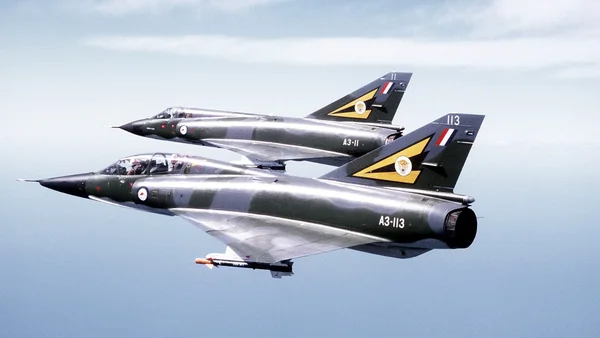 Deux chasseurs Dassault Mirage 2000 en formation dans un ciel bleu, avec un camouflage gris foncé et des marques jaunes et noires sur les stabilisateurs verticaux