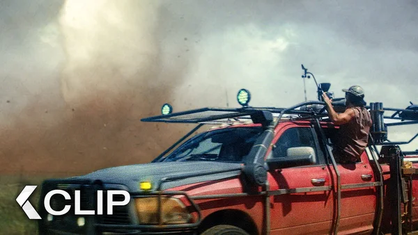 Camionnette rouge traversant un paysage poussiéreux orageux dans le clip Twisters (2024) avec une personne penchée sur la fenêtre passager