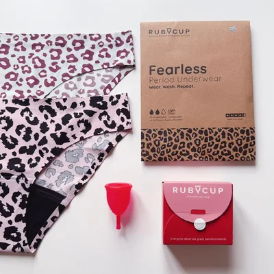 Des sous-vêtements de protection périodique à motif léopard, une coupe menstruelle rouge et leurs emballages de la marque RUBYCUP, sur un fond clair.