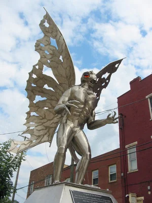 Statue en métal argentée du Mothman, figure ailée et musclée, située devant des immeubles rouges à Point Pleasant, dans le comté de Mason, West Virginia.