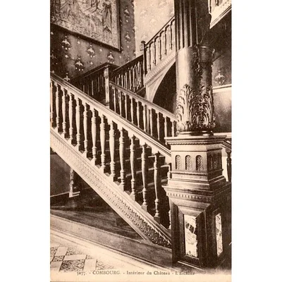 Photographie ancienne en noir et blanc de l'escalier intérieur du château de Combourg, avec une grande colonne sculptée et une rampe en bois.