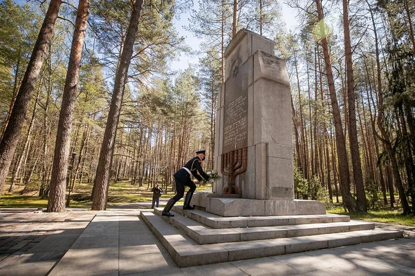 Un garde en uniforme déposant un wreath au pied d'un monument de pierre avec étoile de David et menorah, dans une forêt de pins près de Vilnius, en Lituanie, lors d'une cérémonie commémorative de la Shoah par balles.