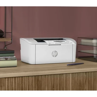 Imprimante laser monochrome HP LaserJet M110w blanche posée sur un bureau en bois, à côté d'une pile de livres et d'un stylo.