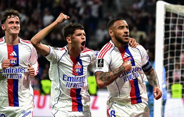 Trois joueurs de football en maillots blancs, rouges et bleus célébrant sur un terrain, avec un joueur criant et levant le poing au centre, après la victoire d'OL contre Rennes